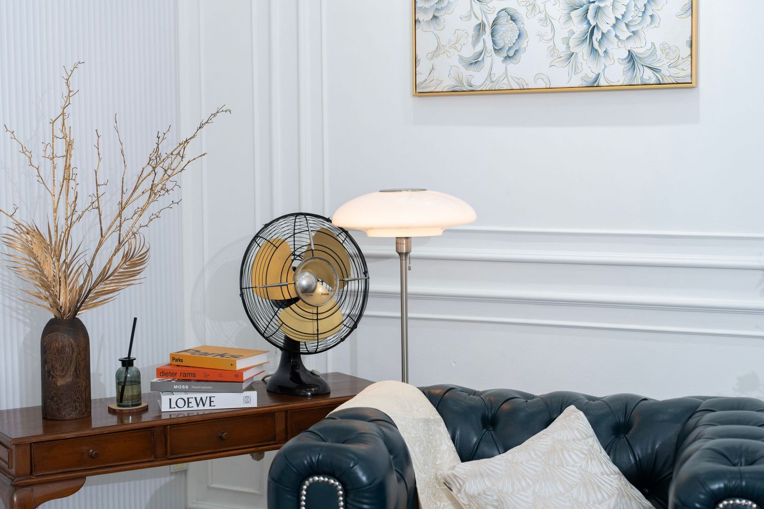 Vintage metal fan and white table lamp on wooden console table with dried pampas grass in modern living room.