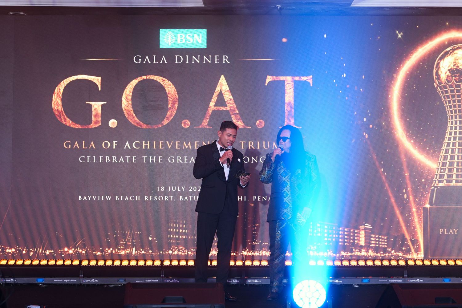 Two presenters on stage at BSN G.O.A.T Gala of Achievement Tribute dinner event.