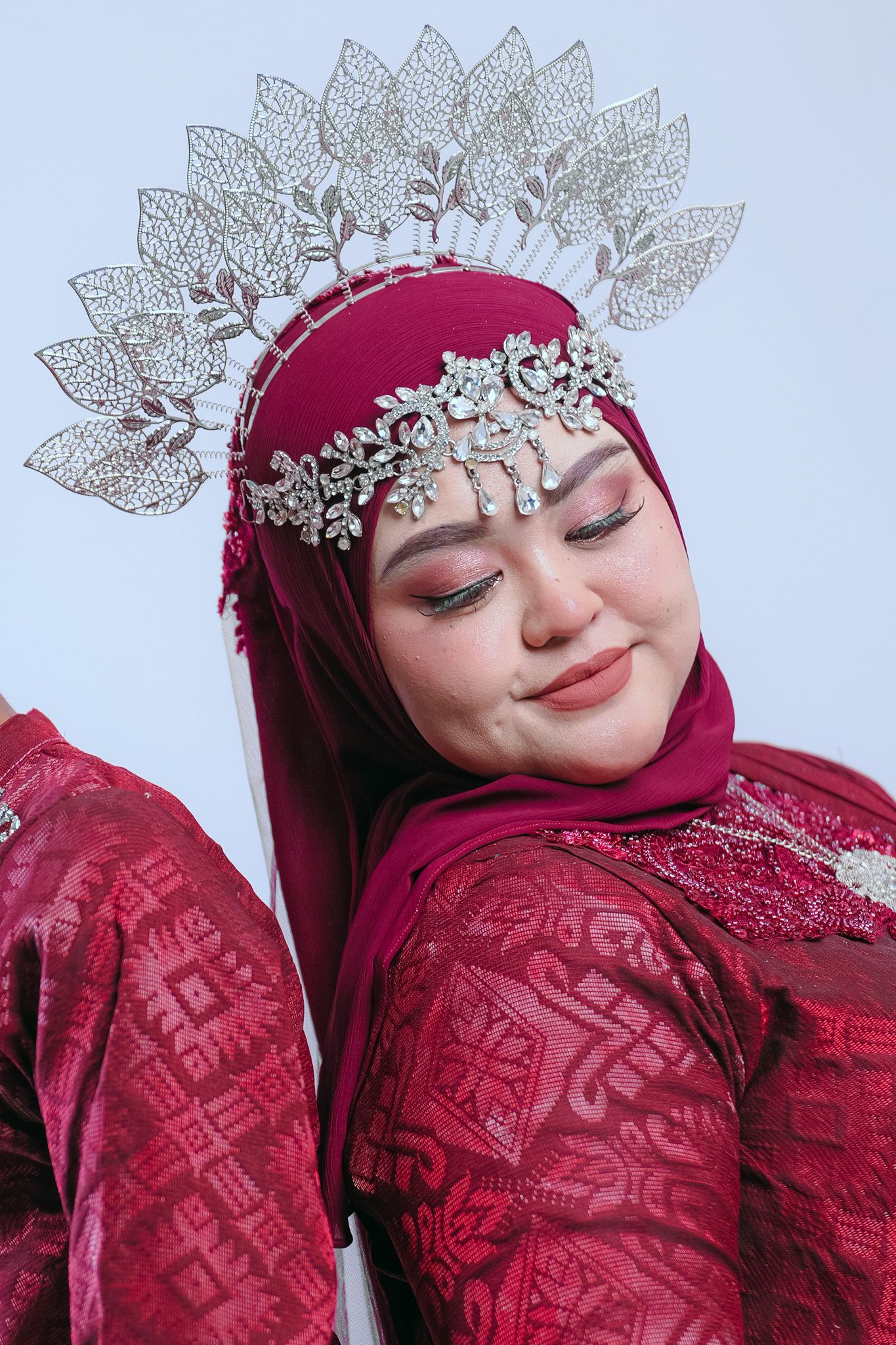 Individual wearing red hijab and ornate silver crown headpiece with delicate leaf details in soft lighting.