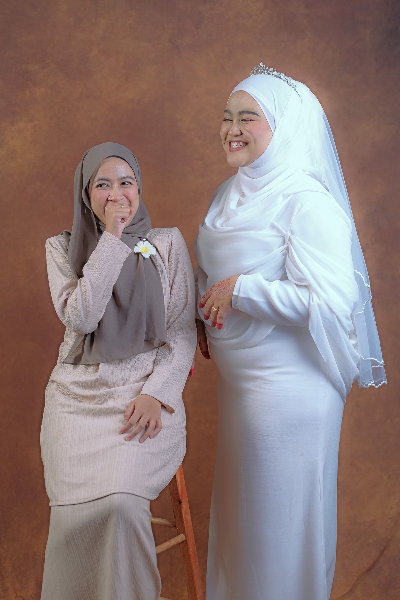 Two women in hijabs sharing a lighthearted moment during formal photo session.