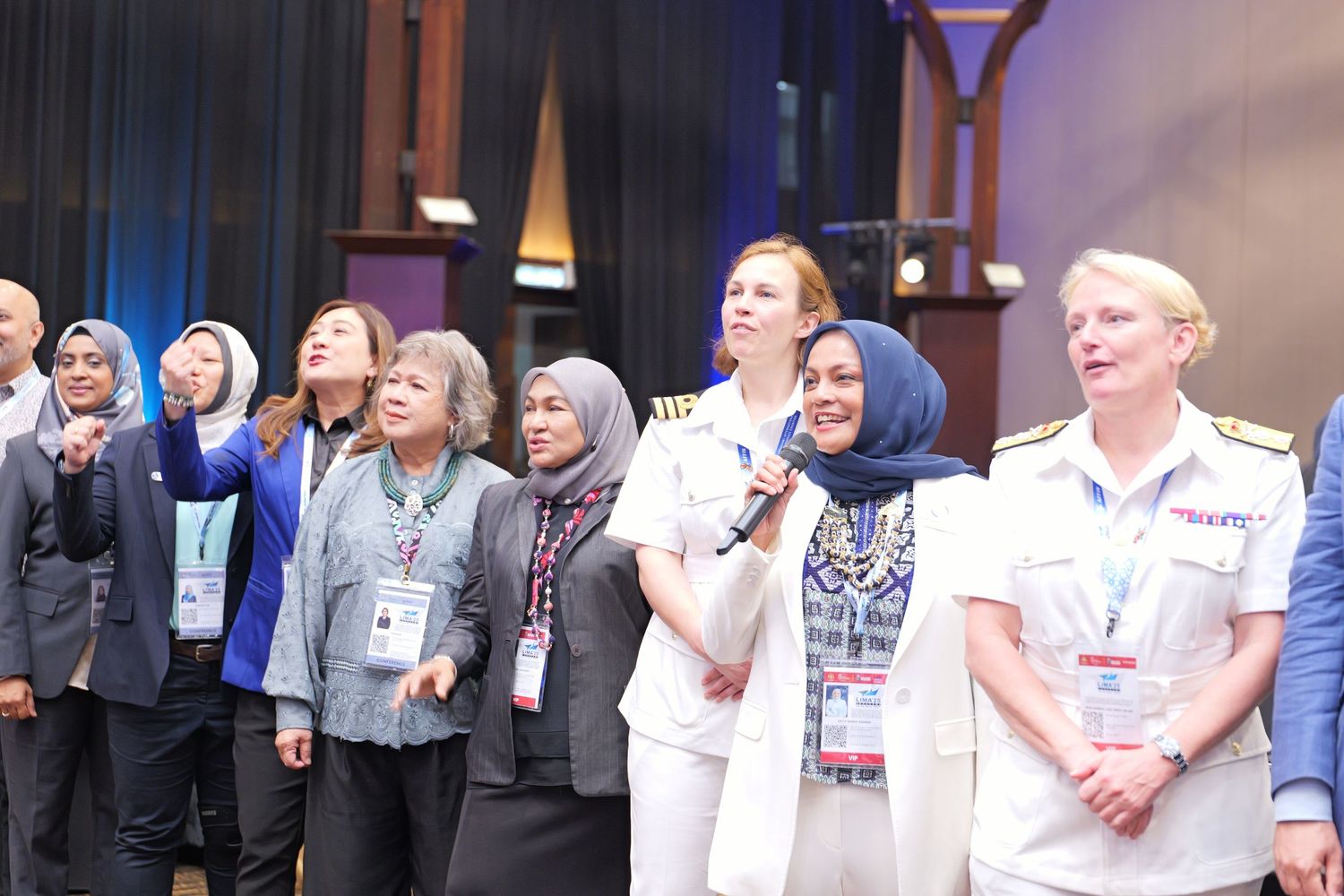 A group of people stand together on stage at what appears to be a conference or event with lighting and decor visible.