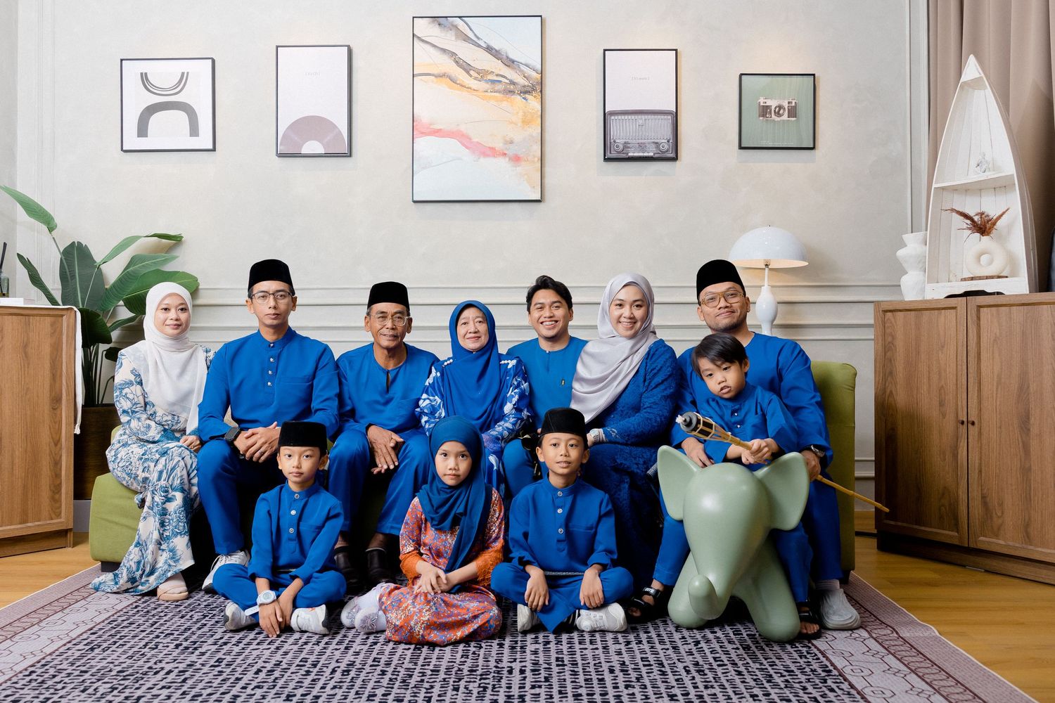 People in matching blue uniforms sit together on the floor of a room with framed artwork on the walls.