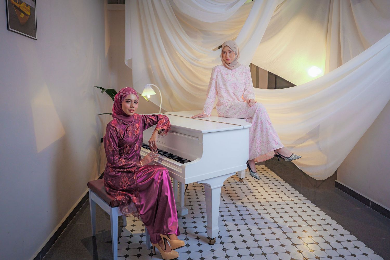 Two people in colorful flowing outfits pose with a white grand piano in a room with draped fabric walls.