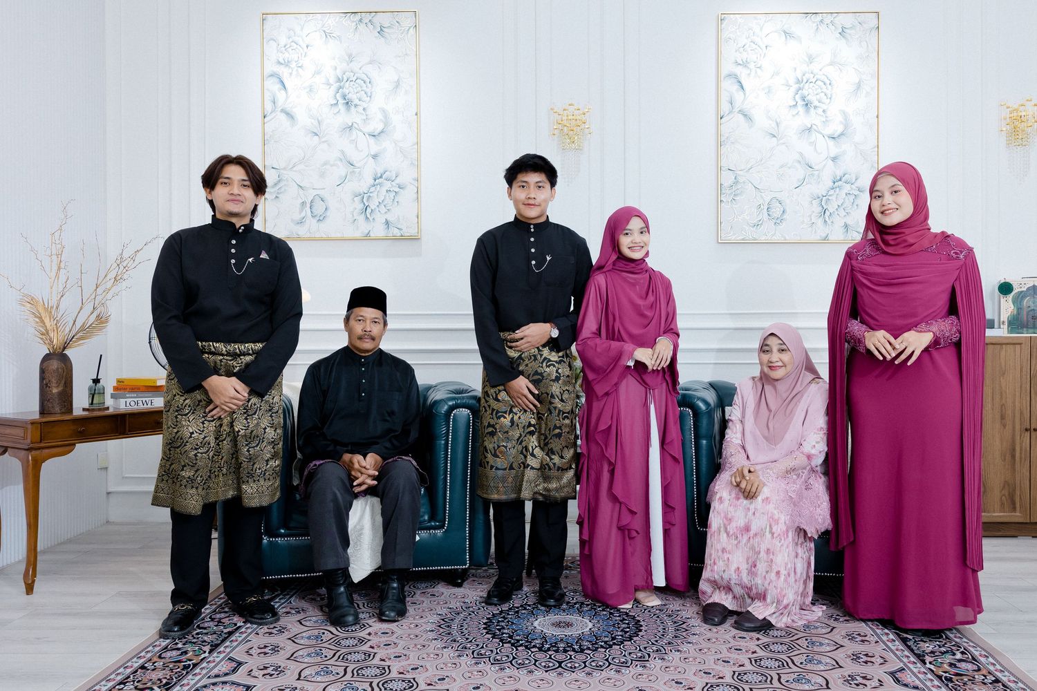 A family group sits together in formal attire against a light colored wall with decorative artwork.
