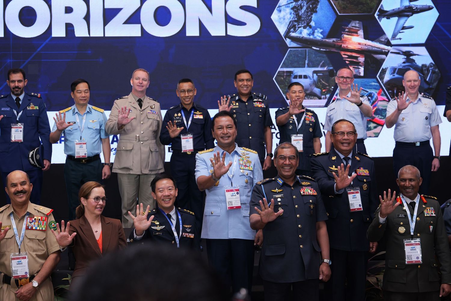 Group of military officials waving at camera during an event with Horizons backdrop.