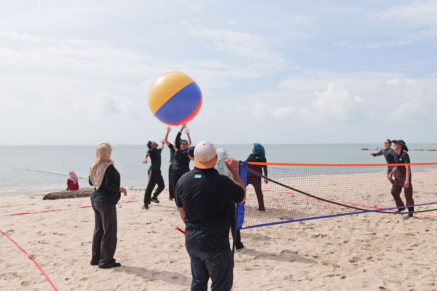 Group of people playing beach volleyball with a colorful oversized ball on a sandy beach by the ocean.