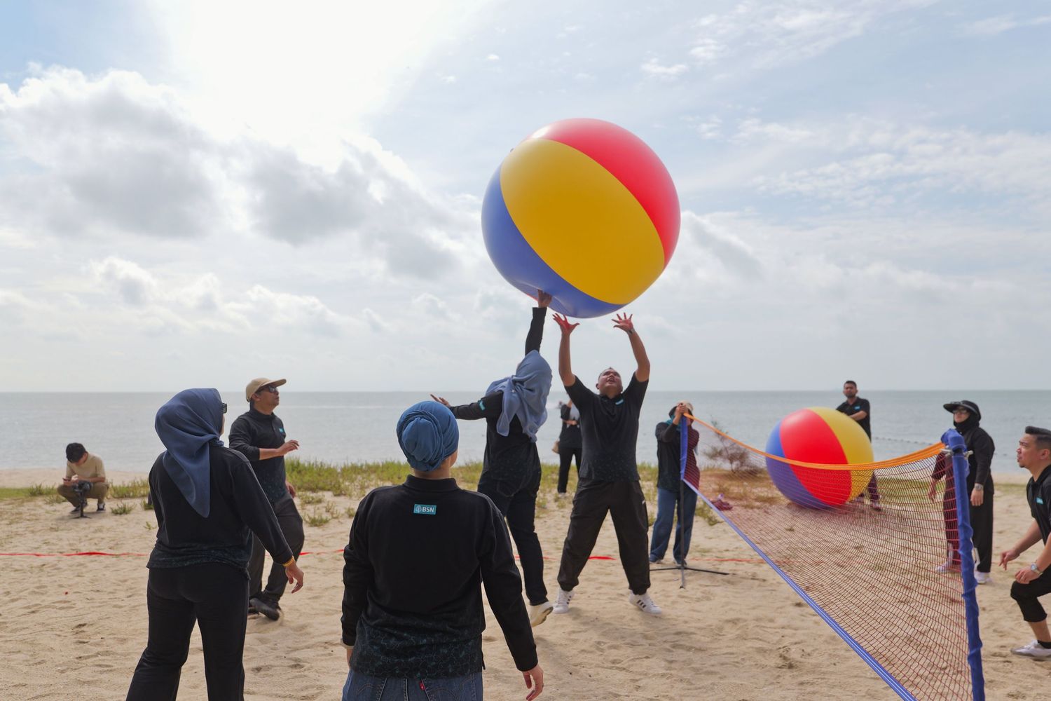 Team building activity with participants playing with large colorful beach ball on a sunny beach.