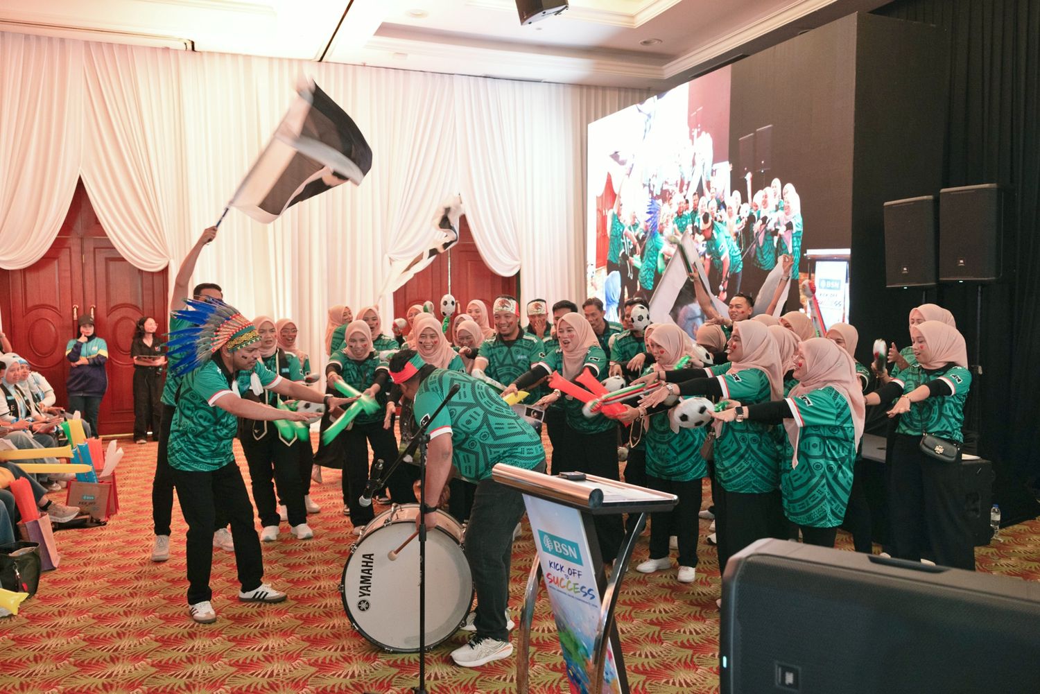 Marching band performing indoors at a sports event with drums and green uniforms.