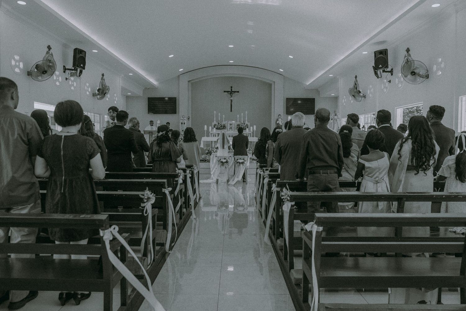 Wedding ceremony taking place in bright church interior with guests seated in wooden pews.