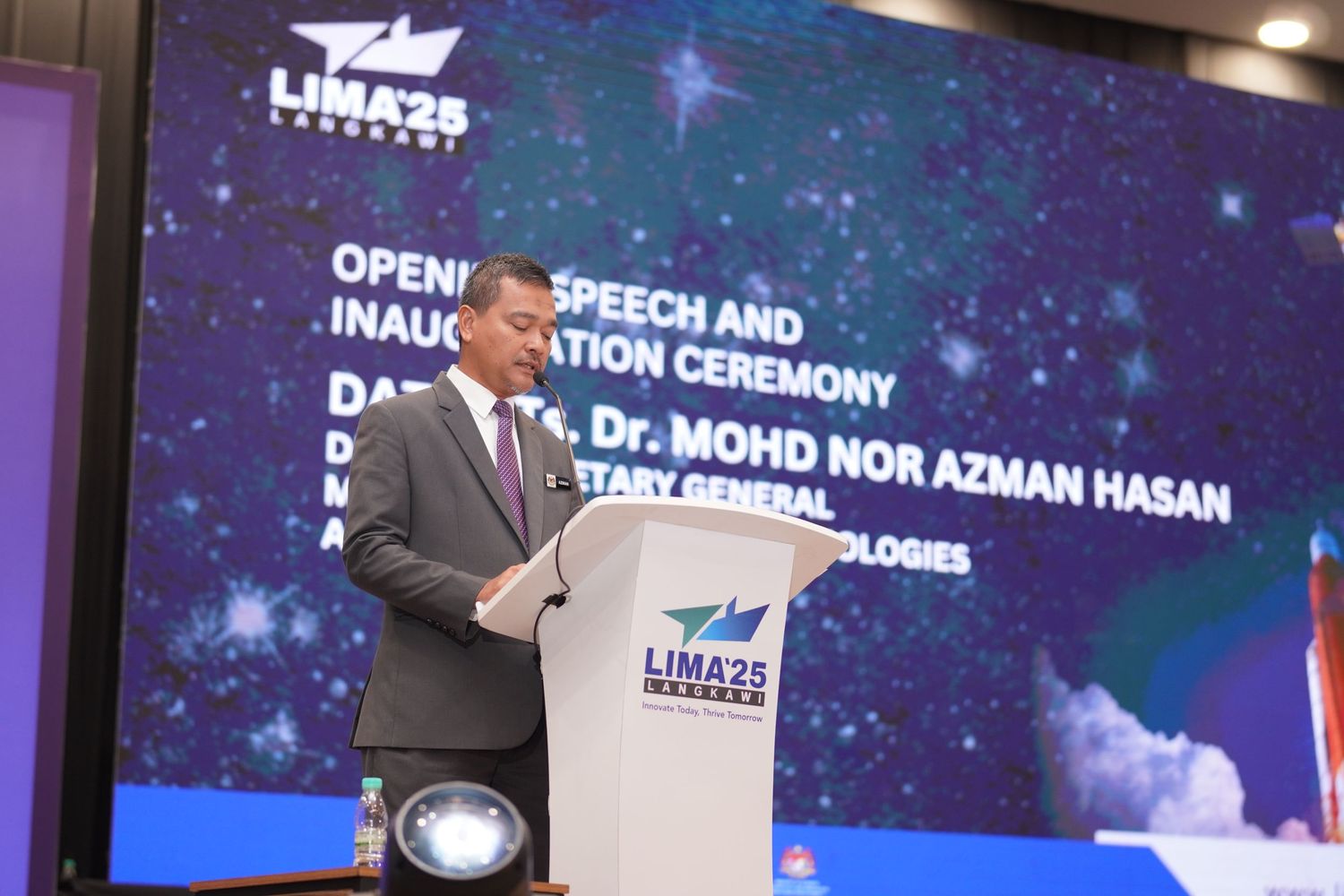 Speaker presenting at LIMA25 inaugural ceremony with cosmic-themed backdrop on stage.