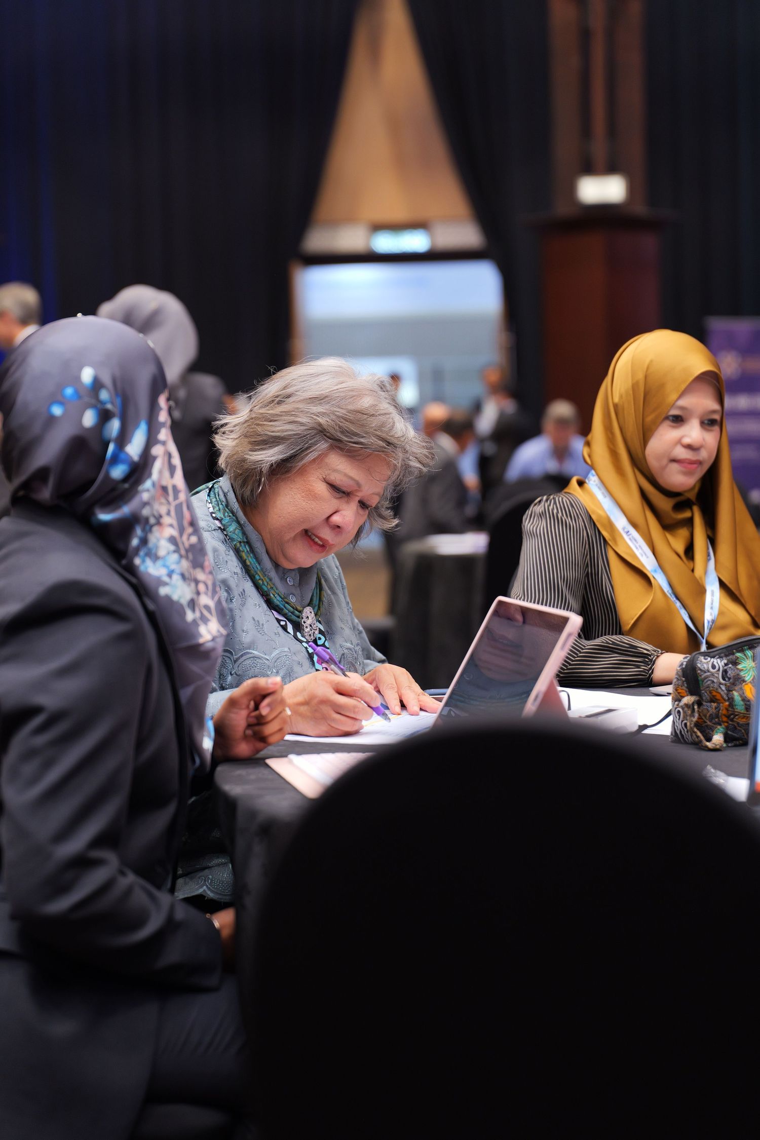 Conference attendees taking notes while sitting at tables during a professional business meeting.
