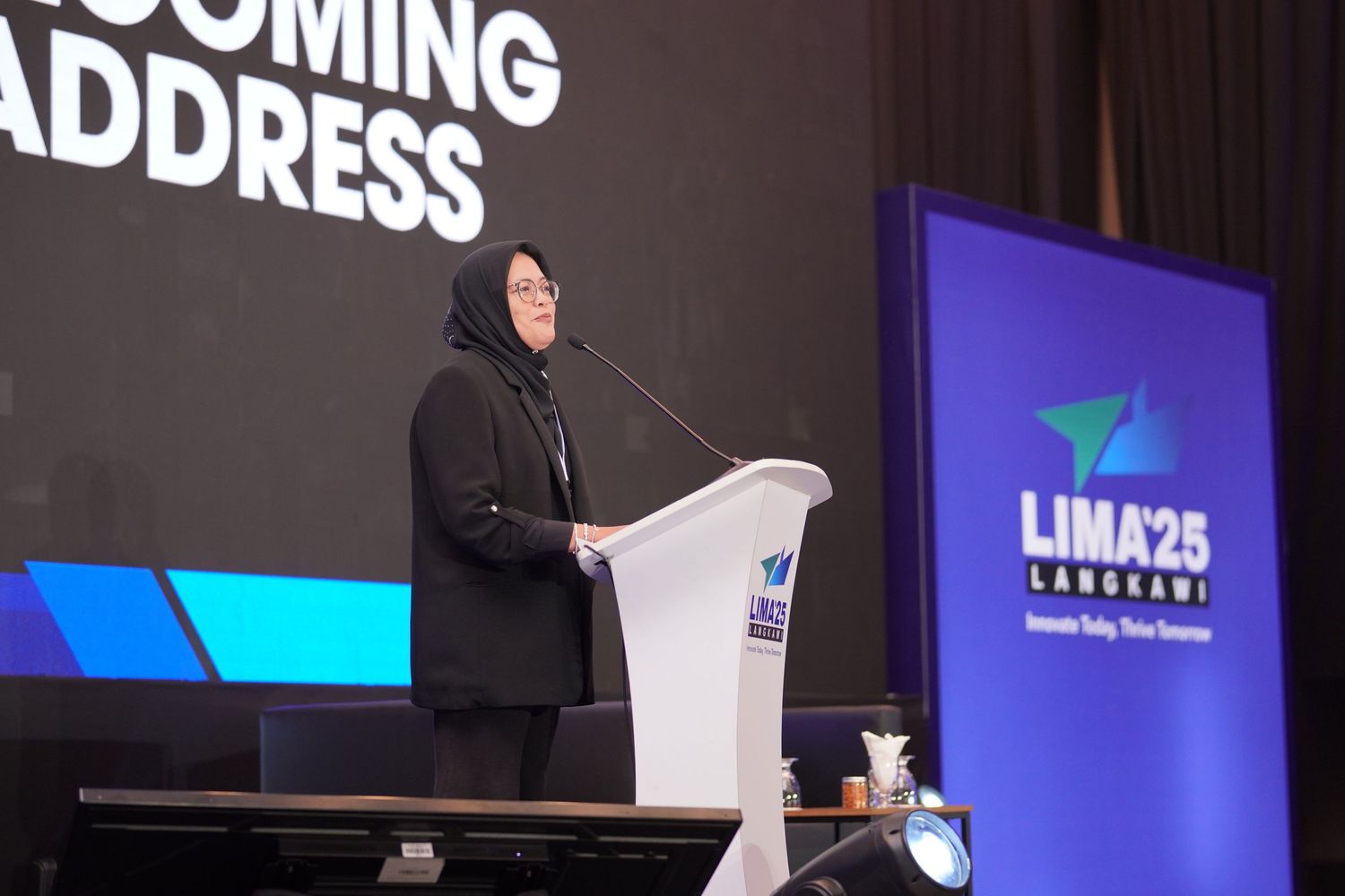 Speaker at podium delivering address at LIMA25 conference with blue branding backdrop.