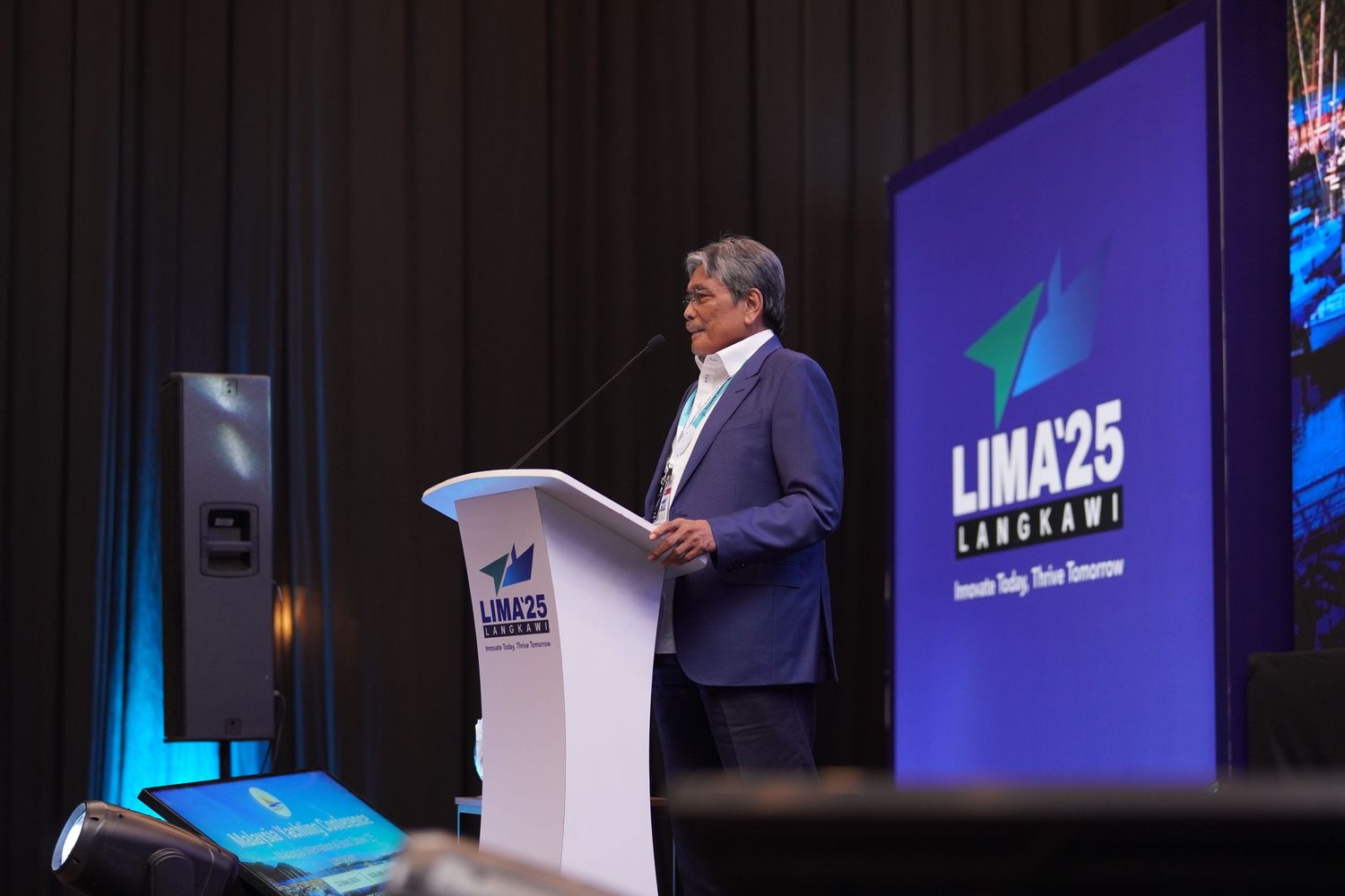 Presenter at white podium with LIMA25 backdrop delivering speech at conference.
