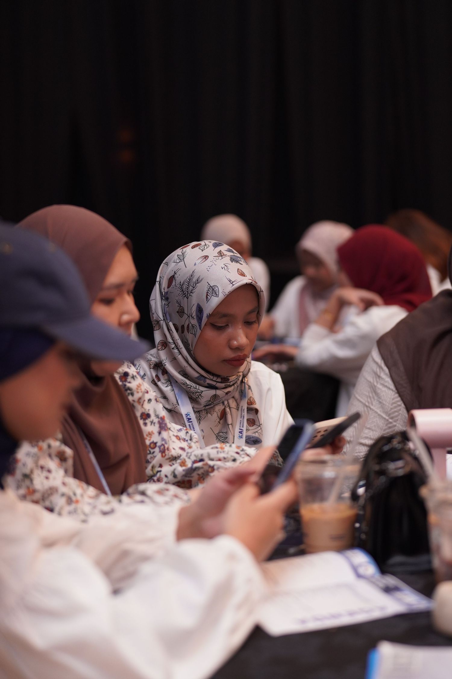 Students in hijabs use mobile phones while sitting together at a table during study or meeting session.