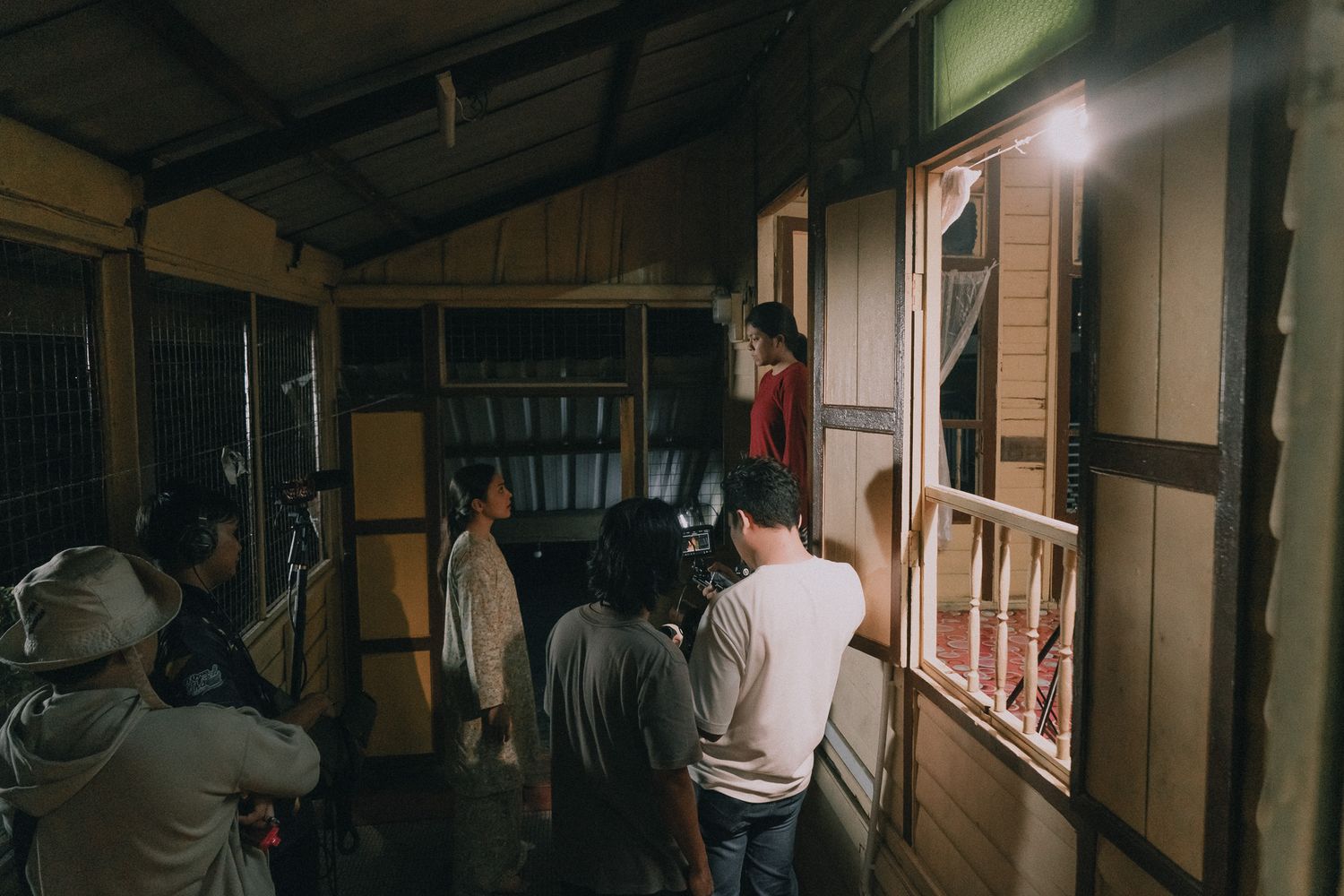People gather in a dimly lit wooden hallway while some individuals climb onto a platform above a traditional doorway.