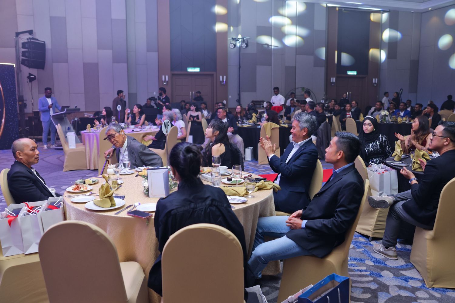 Guests seated at round tables during a formal gala dinner event in a large decorated ballroom.