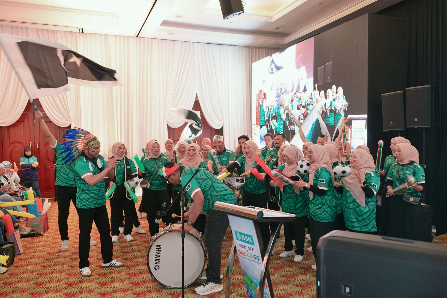 A cheerful group in green jerseys performs with drums at an indoor corporate team building or company event.