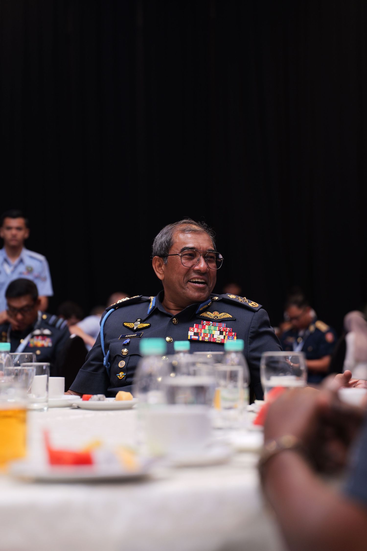 Military officials have a discussion at a formal dining event with drinks on the table.