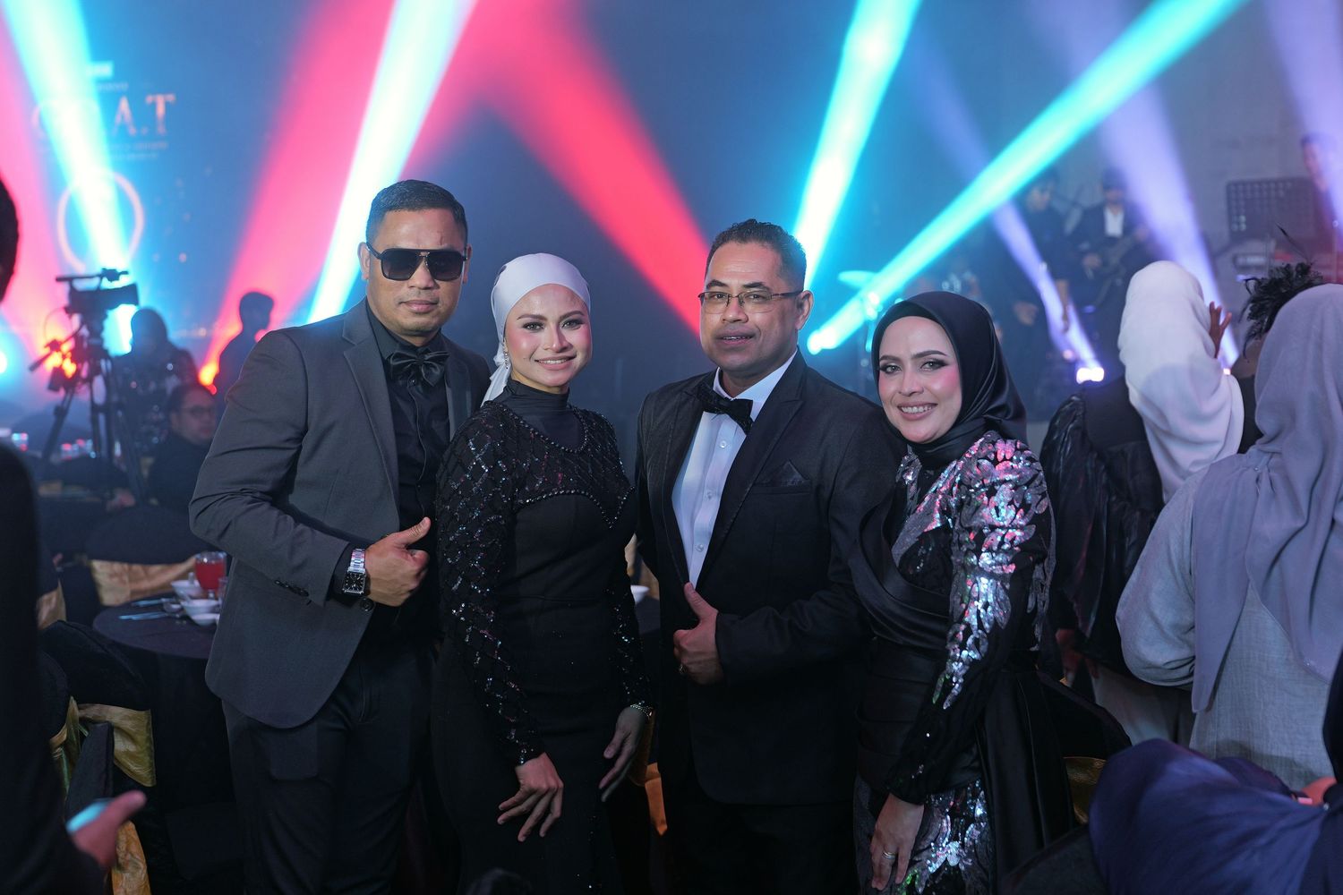 Four elegantly dressed people posing together at a formal evening event with colorful stage lighting.