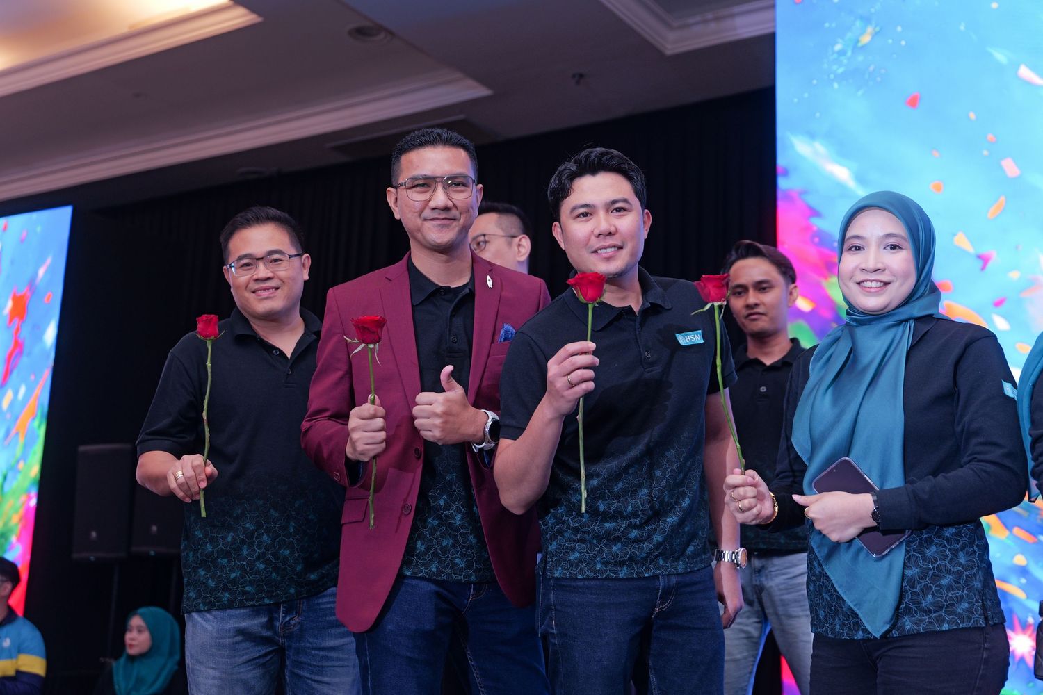 Four professionals holding roses smile together at a colorful corporate celebration event.