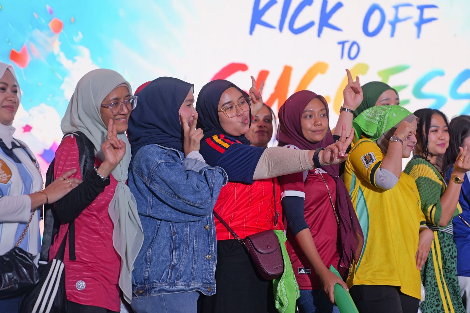 Group of women in colorful hijabs posing and pointing at a Kick Off to Success event banner.