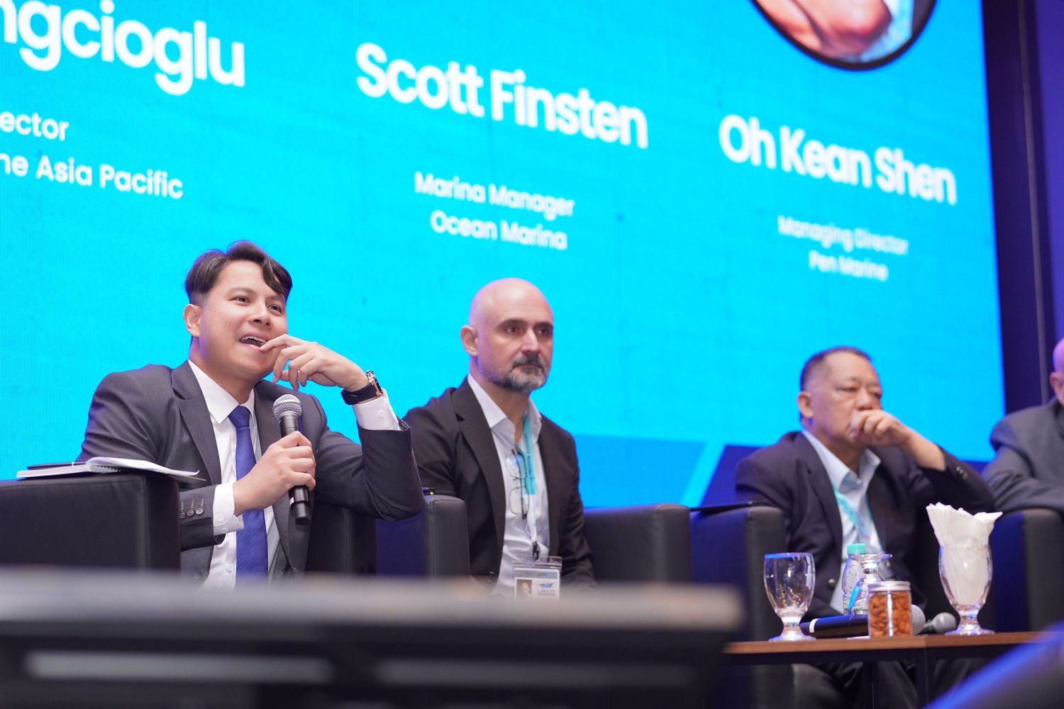 Panel discussion with three speakers at conference table with blue digital display.