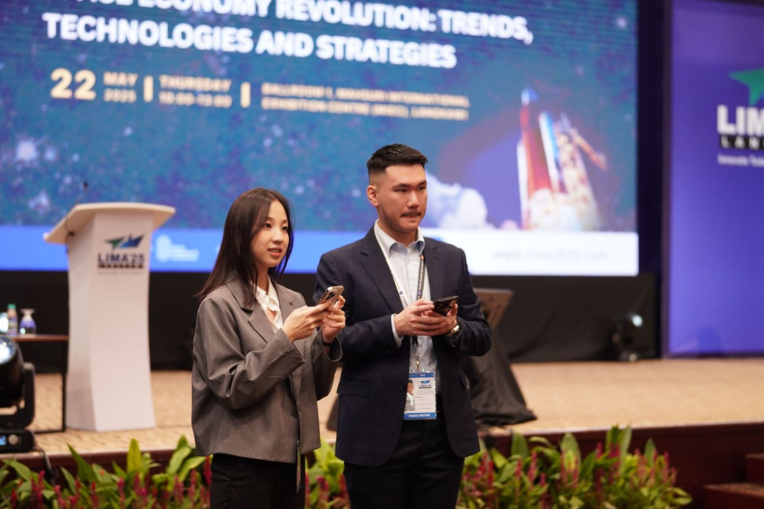 Two presenters sharing the stage at a technology conference with blue digital display screens in the background.
