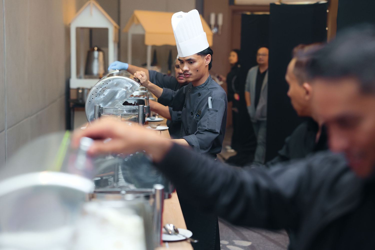 A chef in a white hat serves food at a catering buffet during a corporate dinner event.