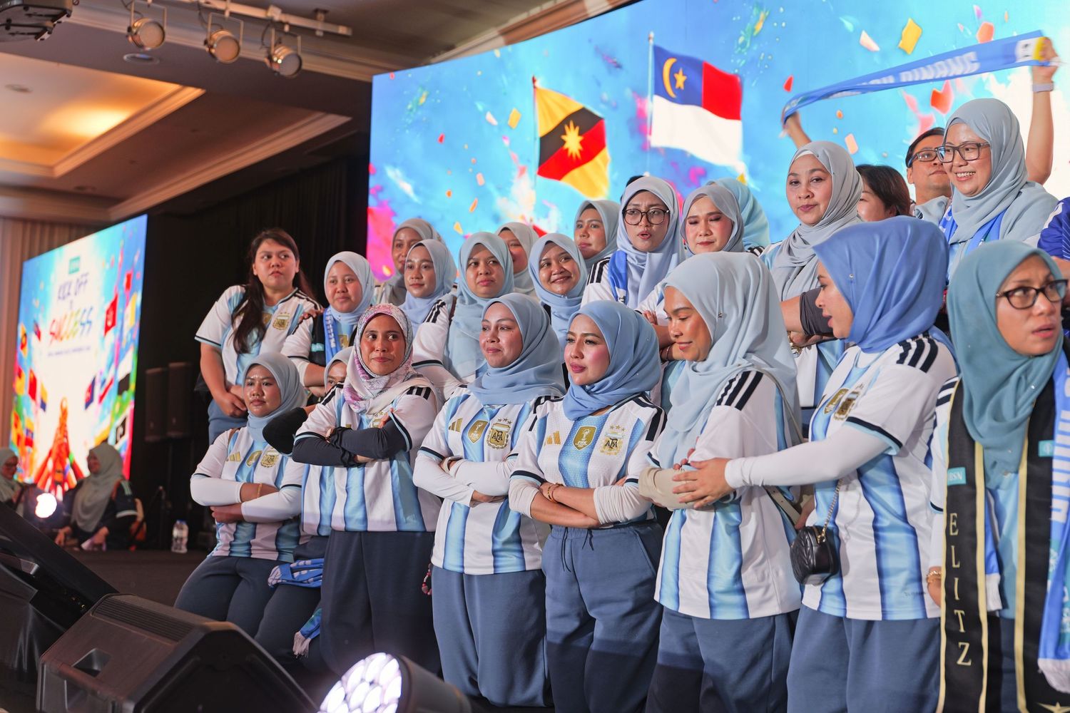 Group of women wearing hijabs and Argentina soccer jerseys posing on stage at an international event.
