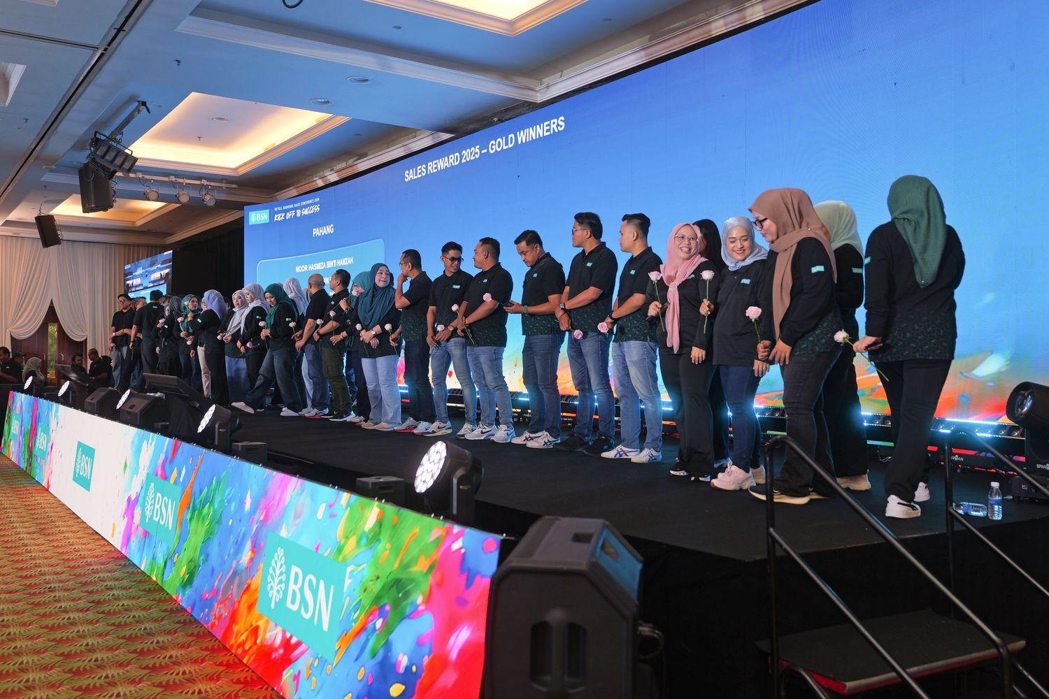 Group of employees in black uniforms standing on stage at a BSN corporate awards ceremony.