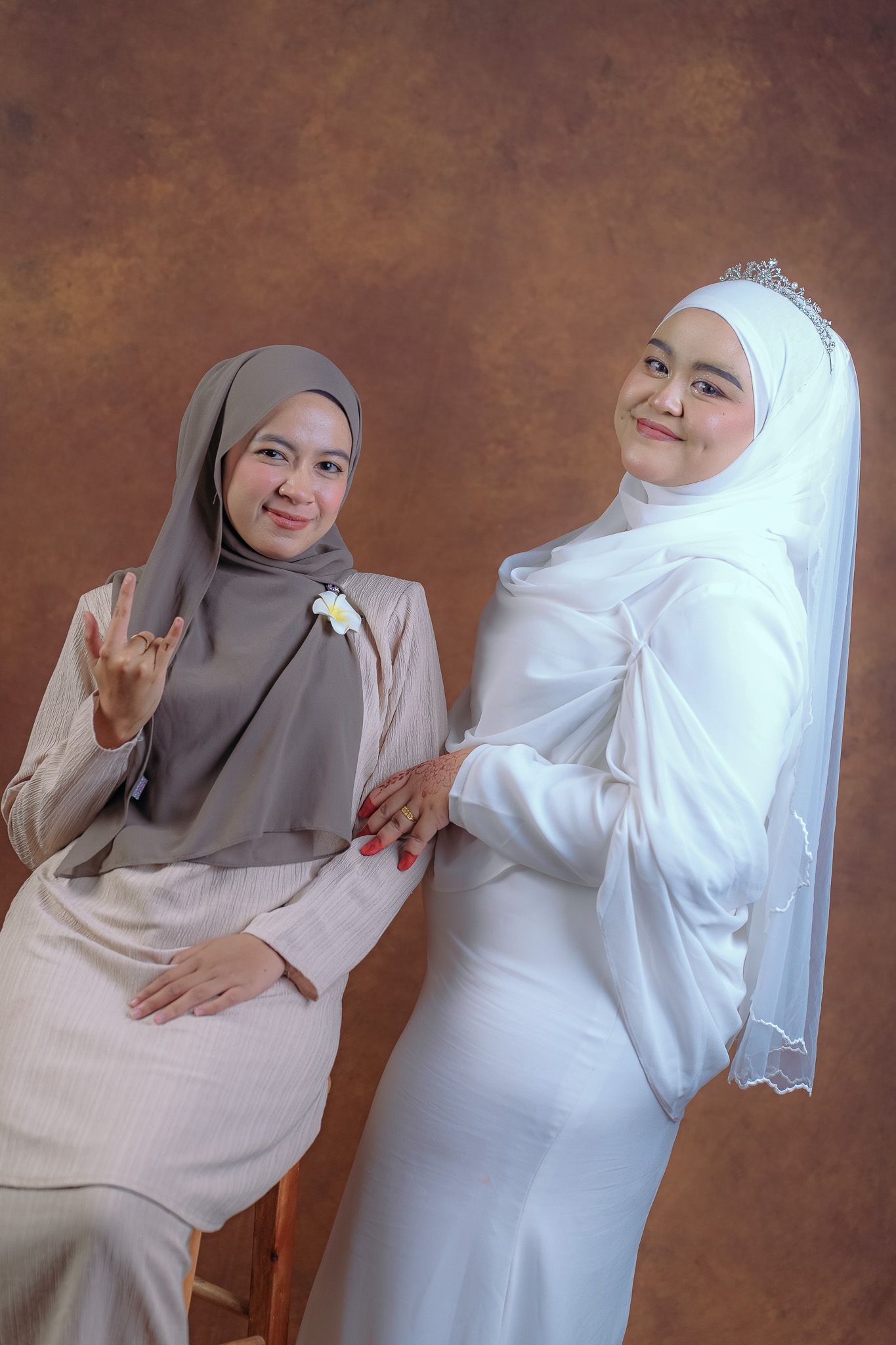 Intimate photoshoot with couple in white and grey Islamic dress posing against brown studio backdrop.