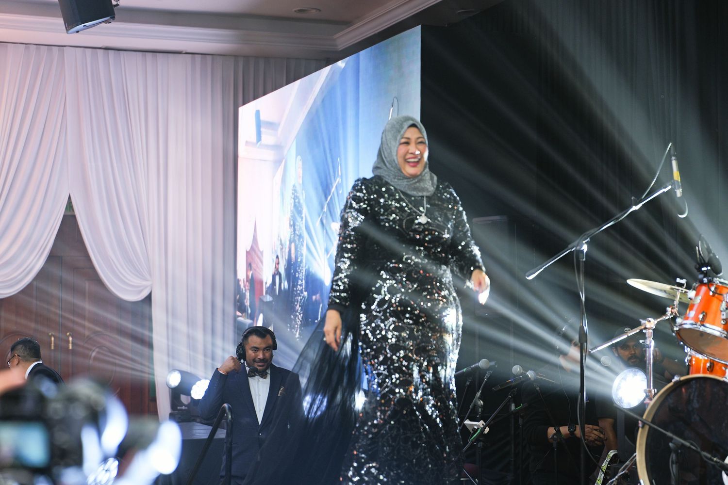 Female performer in sparkling silver gown singing on stage at a formal gala event.