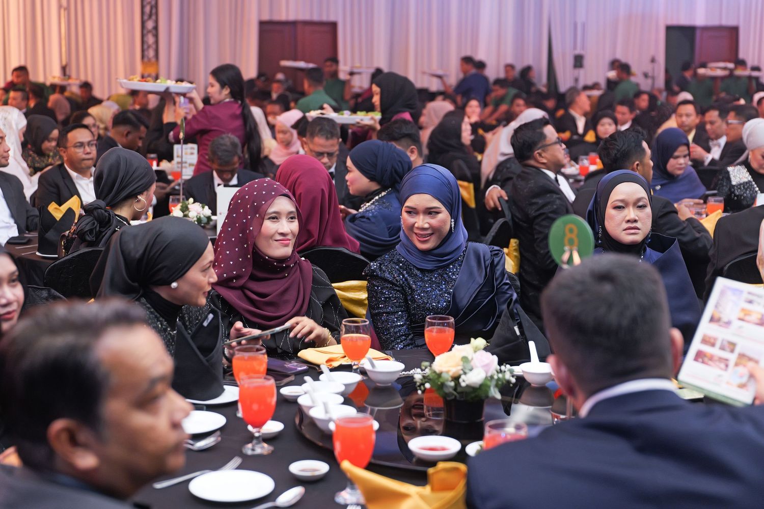 Diverse group of guests in traditional and formal wear socializing at a Malaysian banquet dinner event.
