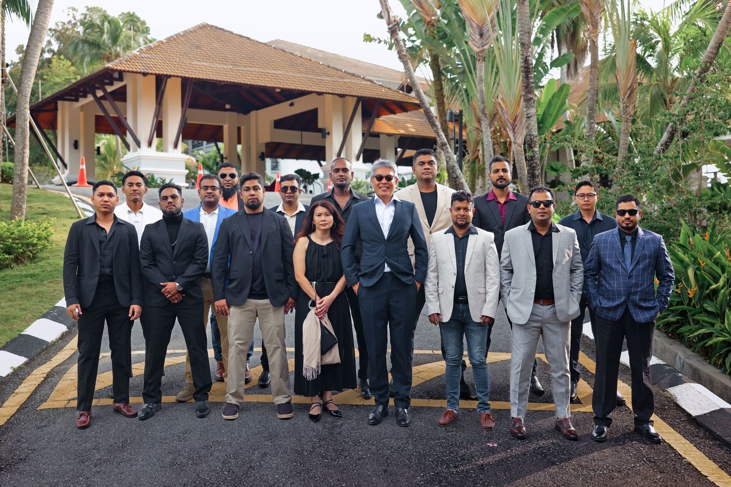 Group of professionals in formal attire posing together at a tropical resort entrance.