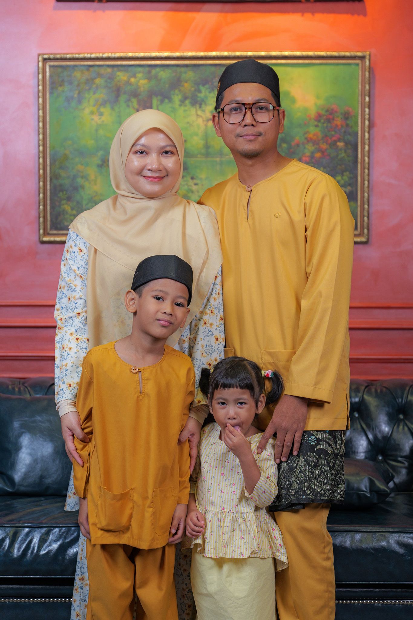 Family wearing coordinated yellow and white outfits poses together on black leather couch against red wall.