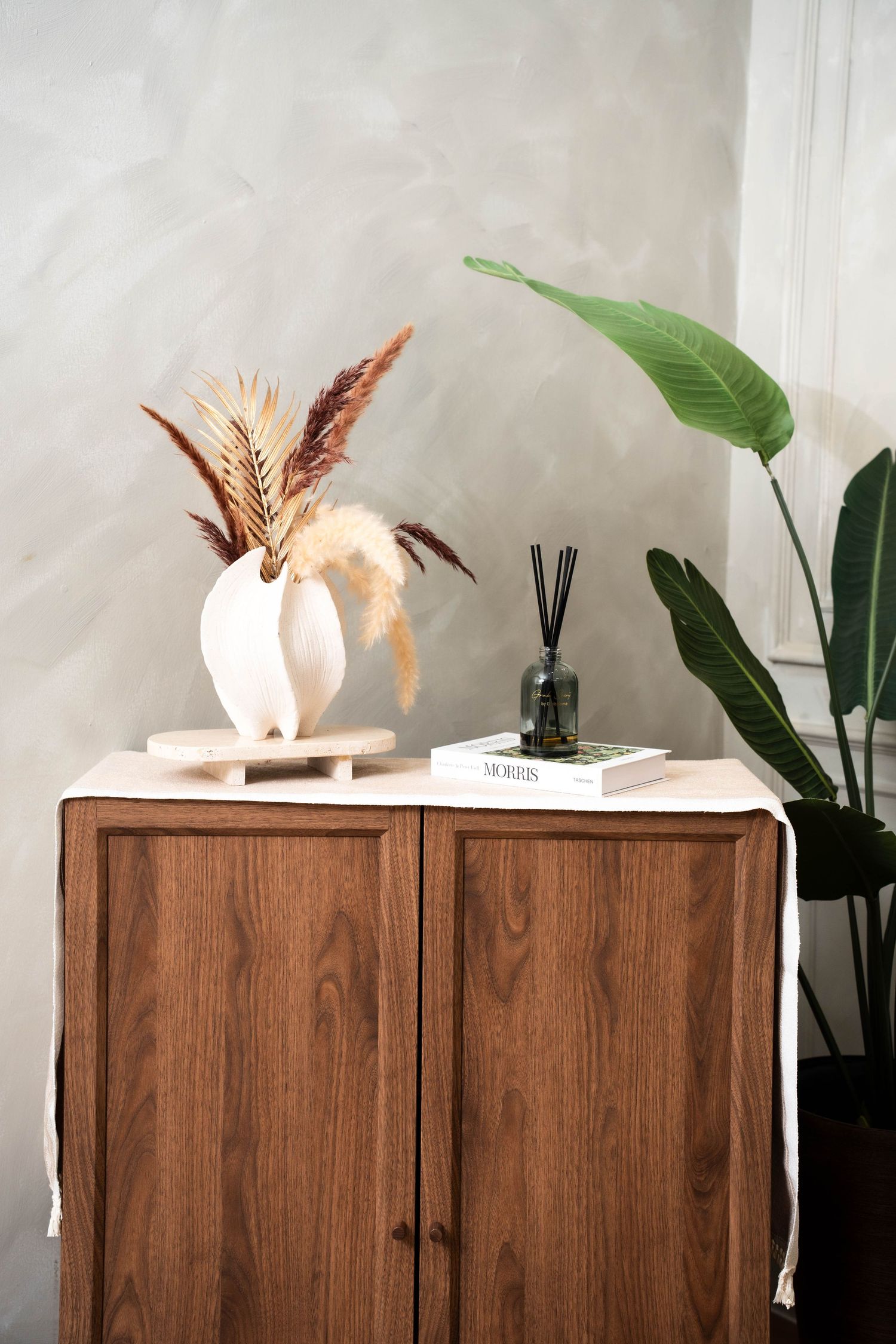 Wooden cabinet with decorative dried flowers and greenery displayed on top against a light colored wall.