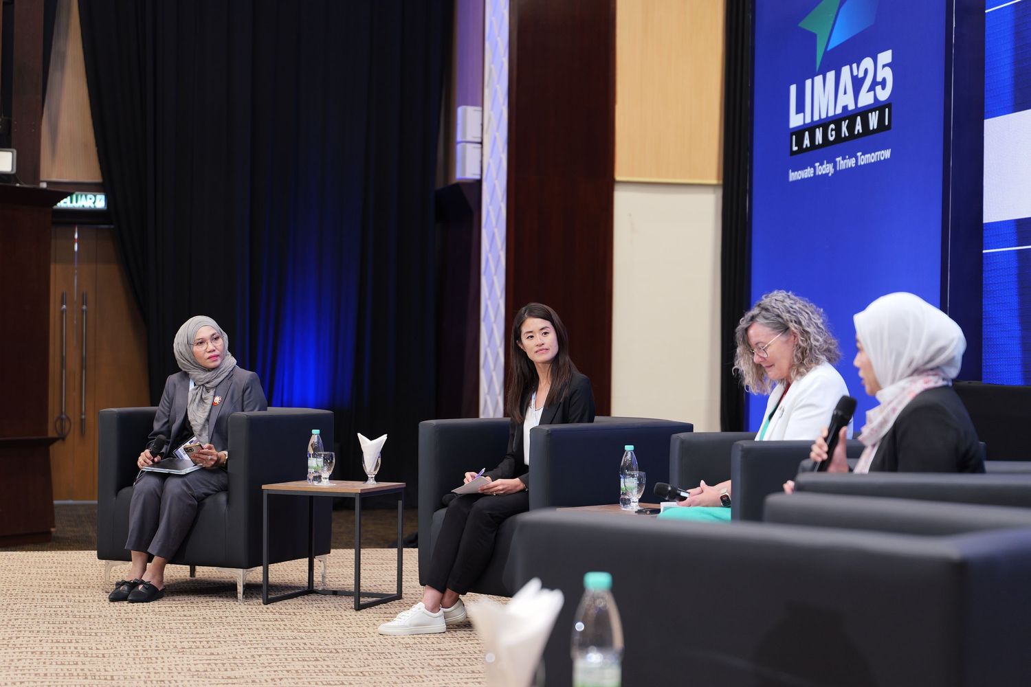 Professional panelists engaged in discussion at a conference with modern stage lighting.