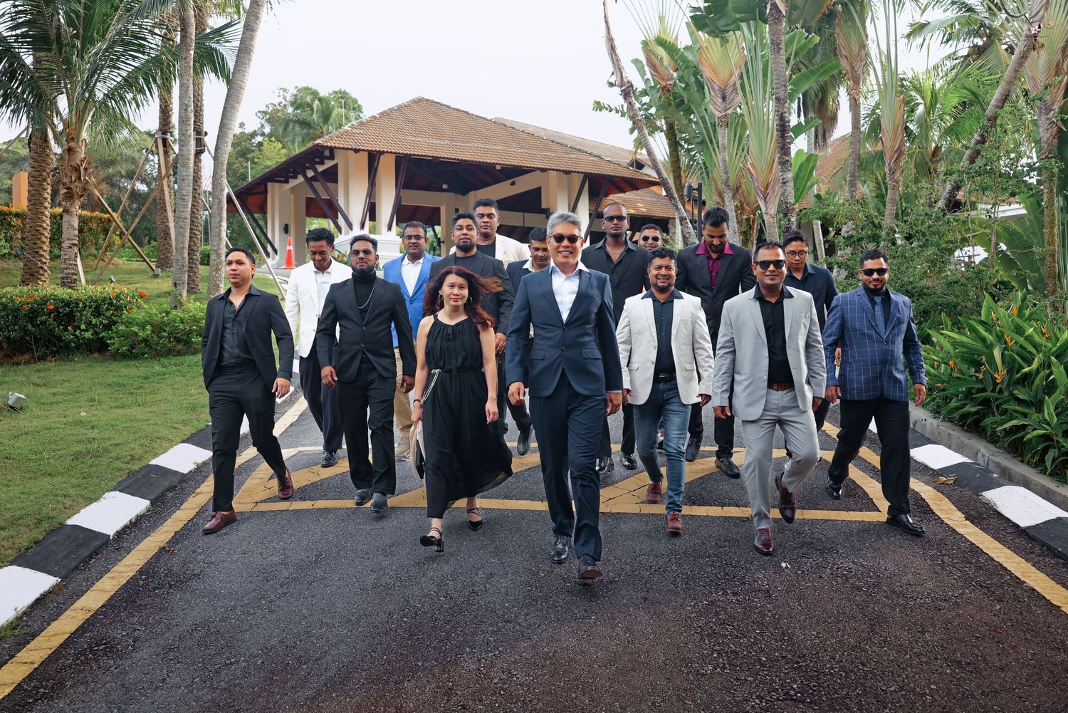Business group walking confidently down a tropical resort driveway in formal wear.