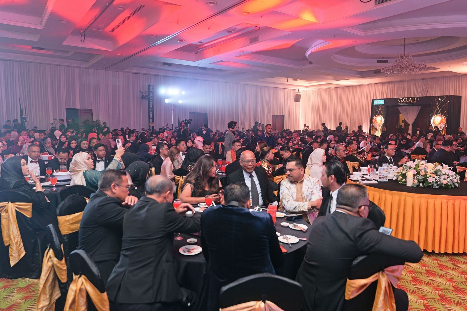 Large formal banquet hall filled with guests seated at round tables during a corporate gala dinner.