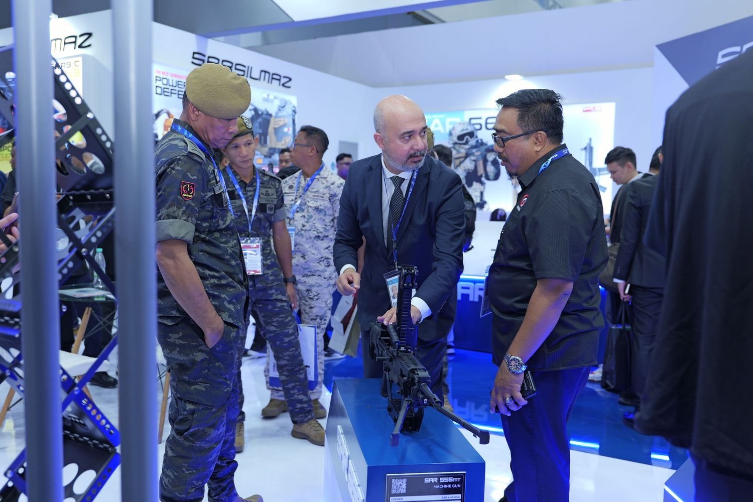 Military personnel and business professionals examining weapons and equipment at a defense industry trade show display.
