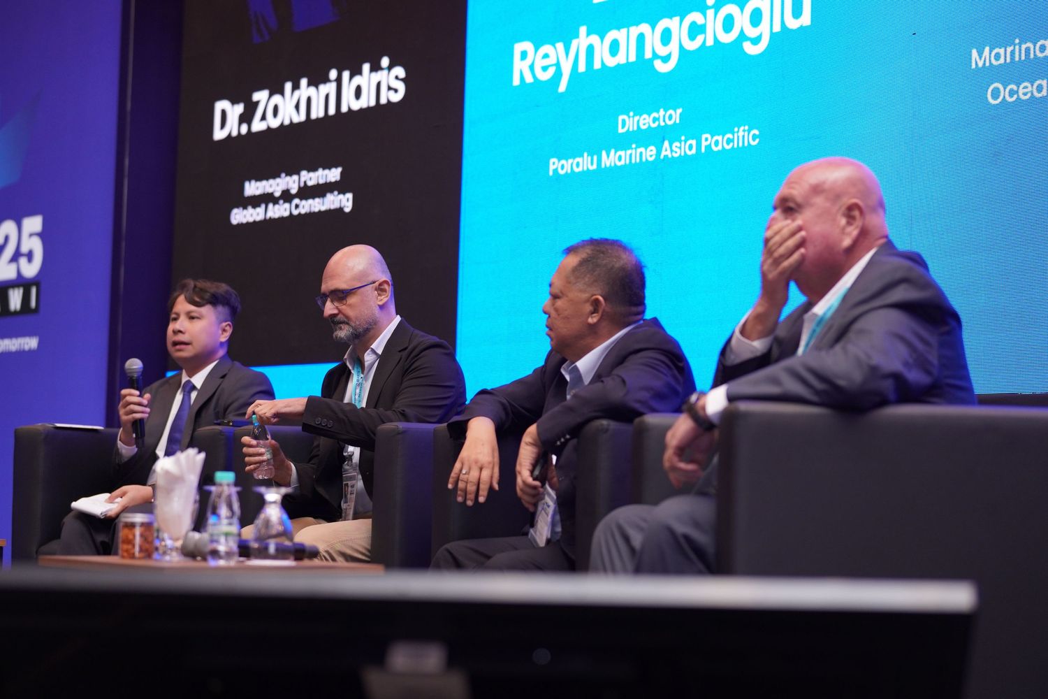 Panel of executives seated on stage during business conference discussion.