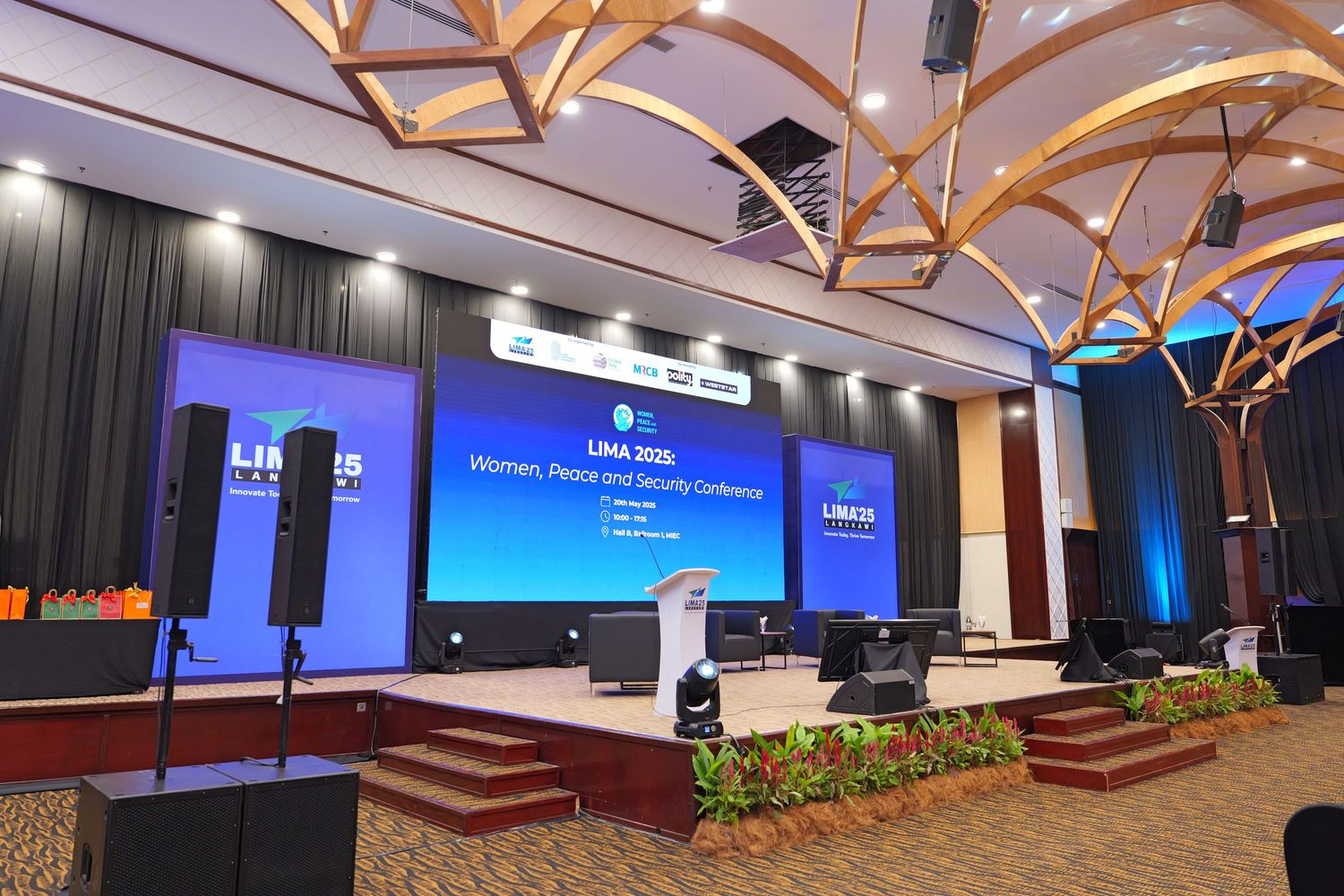 Conference stage with large display screens and wooden beam ceiling design illuminated by blue lighting.