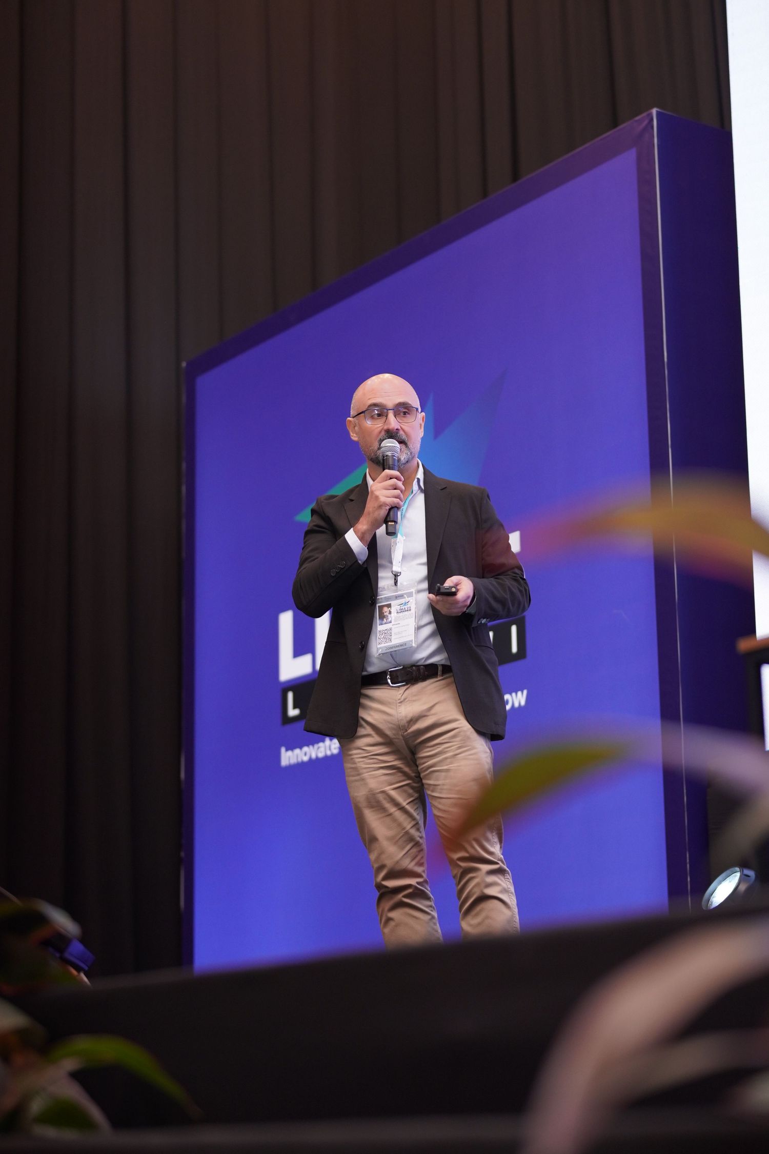 Speaker presenting on stage with purple backdrop at professional conference event.