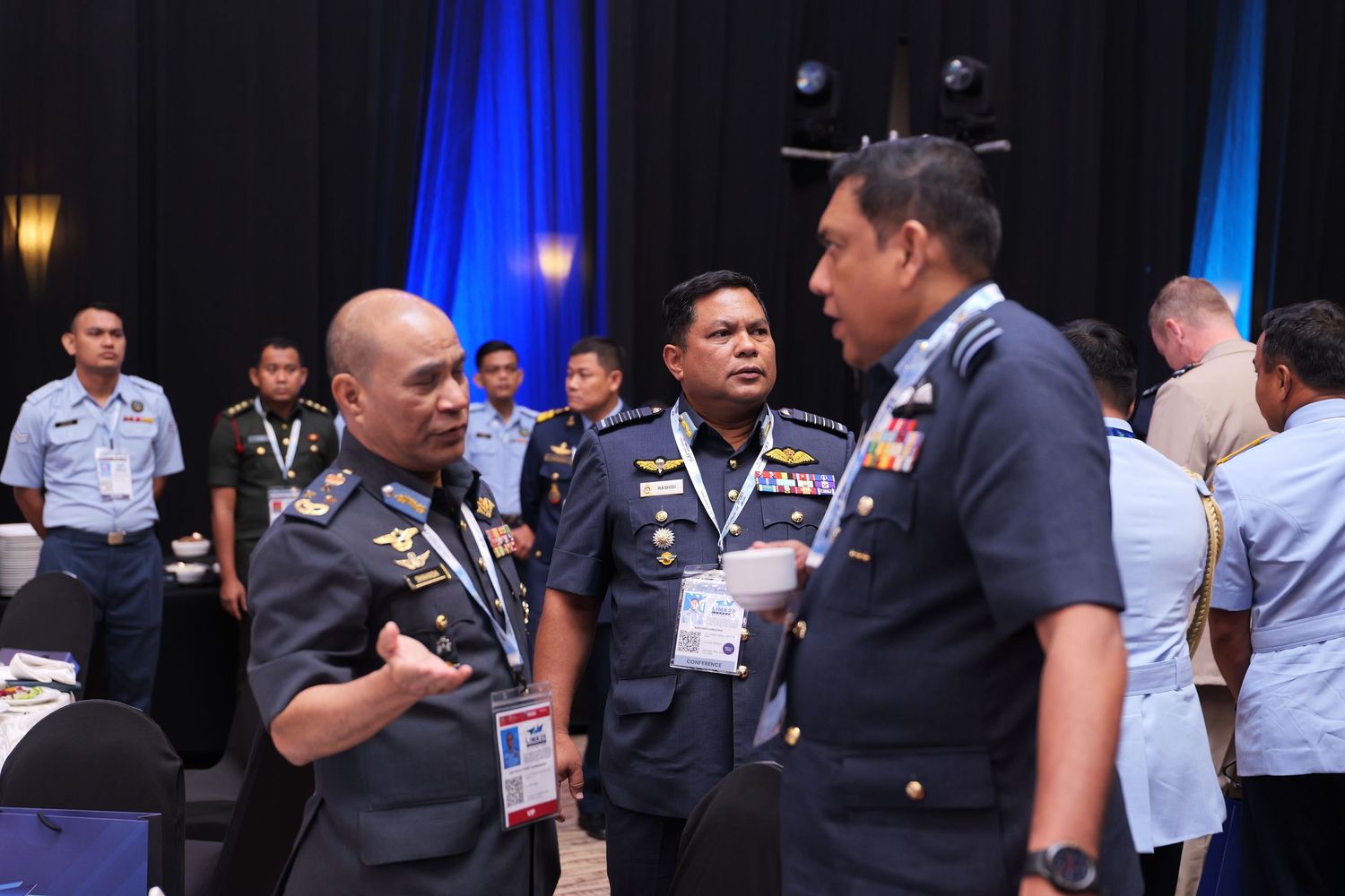 Military and uniformed personnel gather during a formal conference event with blue lighting in the background.