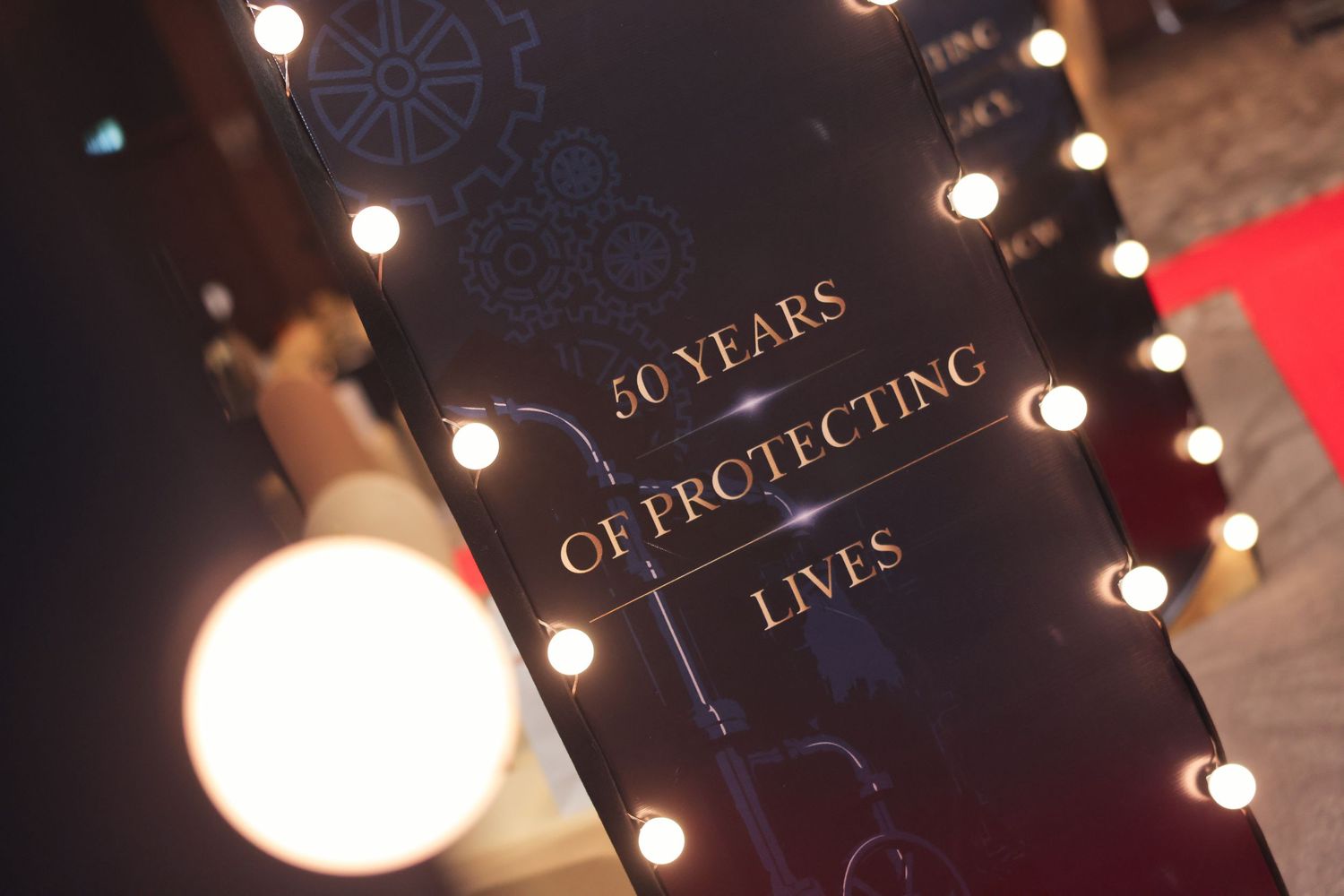 Illuminated sign celebrating 50 years of protecting lives at a formal anniversary event.