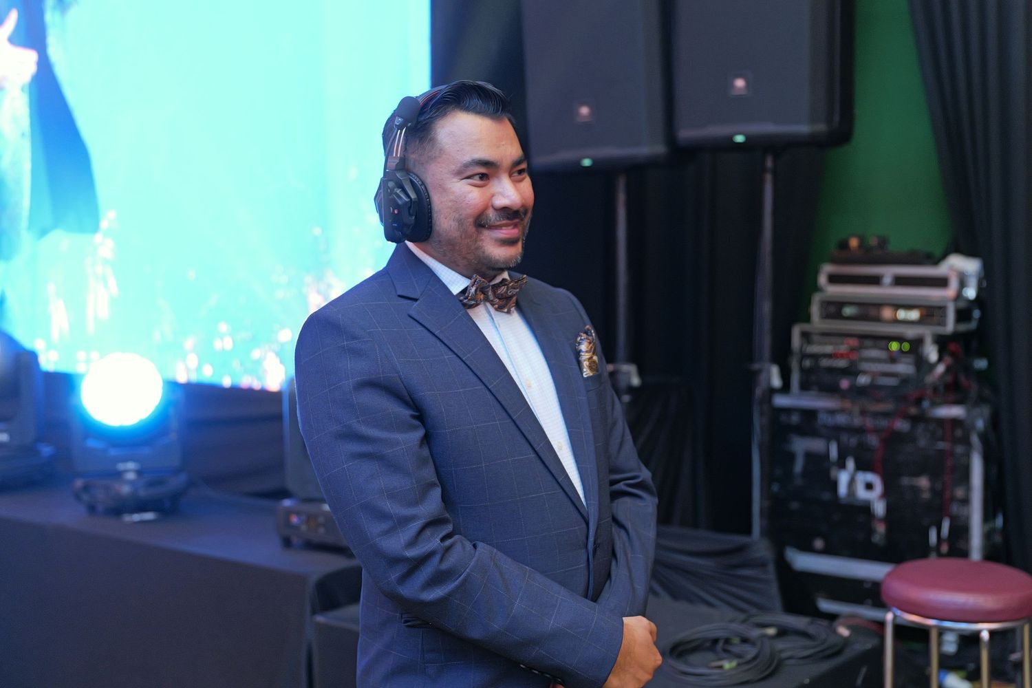 Smiling male DJ in blue suit with headphones at a corporate gala event.