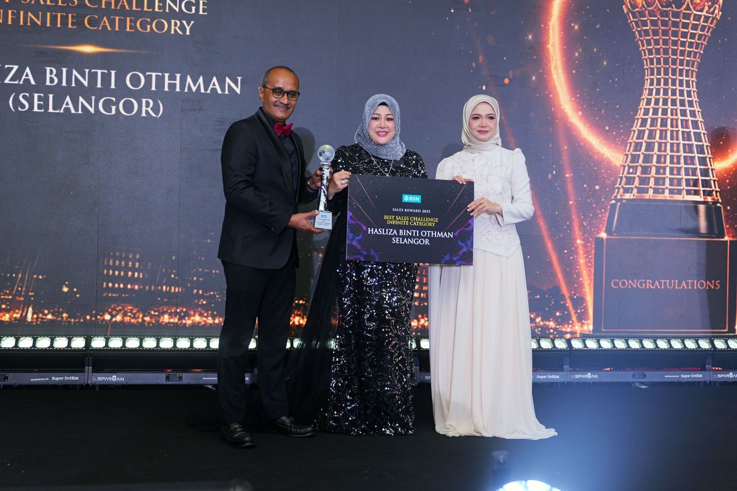 Three people pose together on stage during an awards ceremony, holding a trophy and plaque.