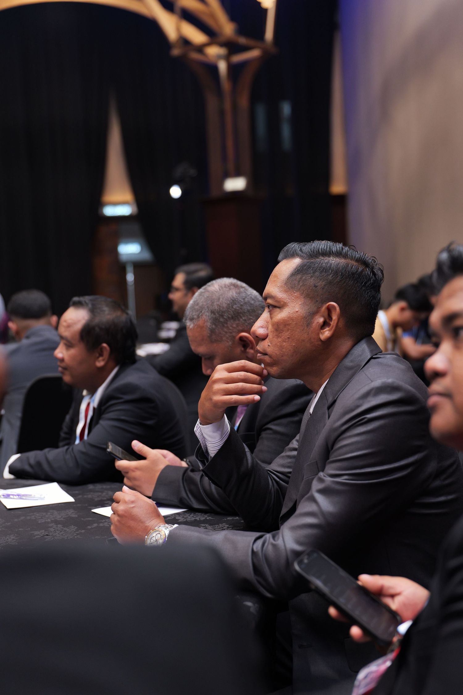 Row of business professionals in suits seated at conference table during formal meeting presentation.