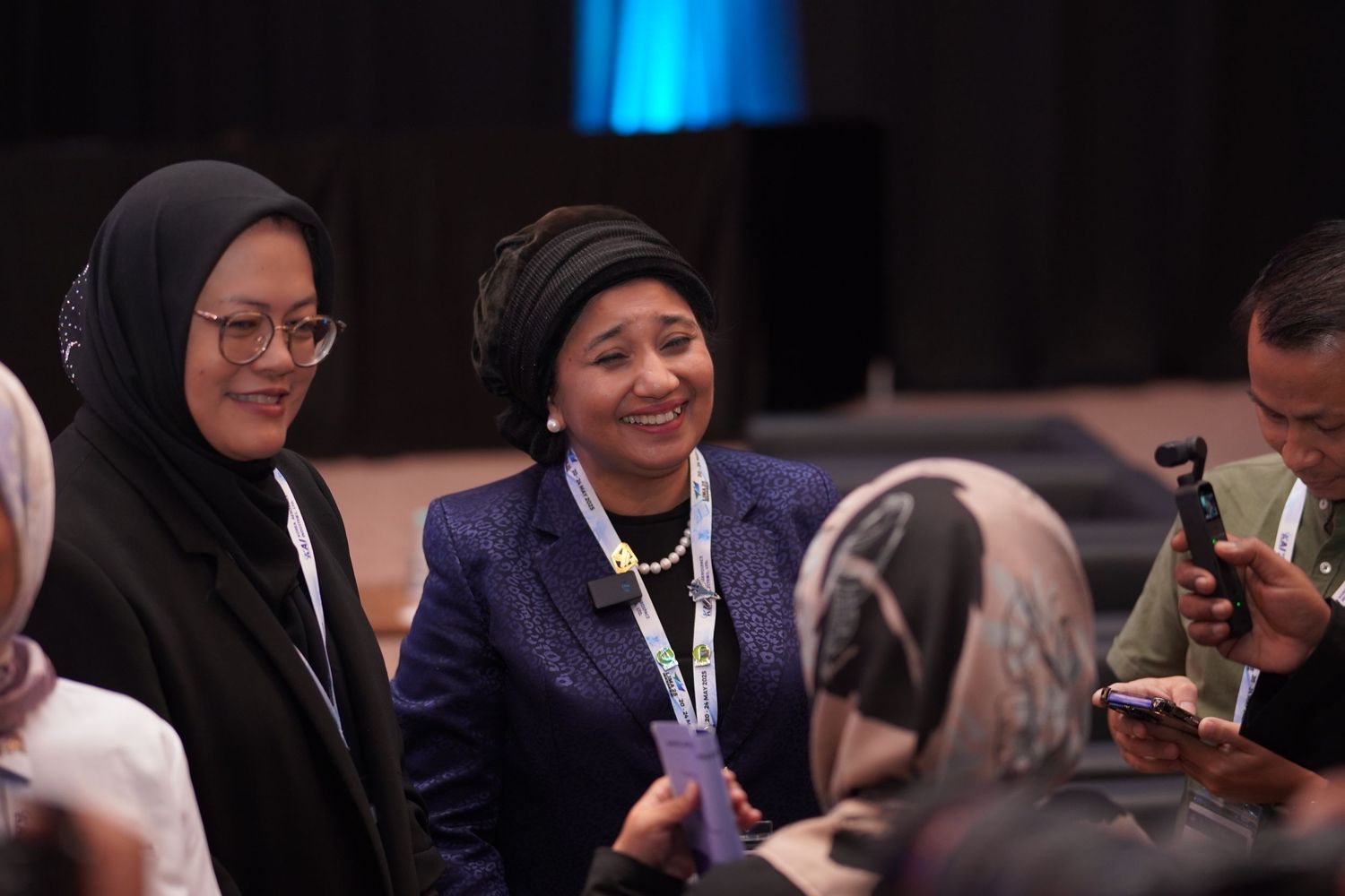 Conference attendees in hijabs smiling and engaging during event session.