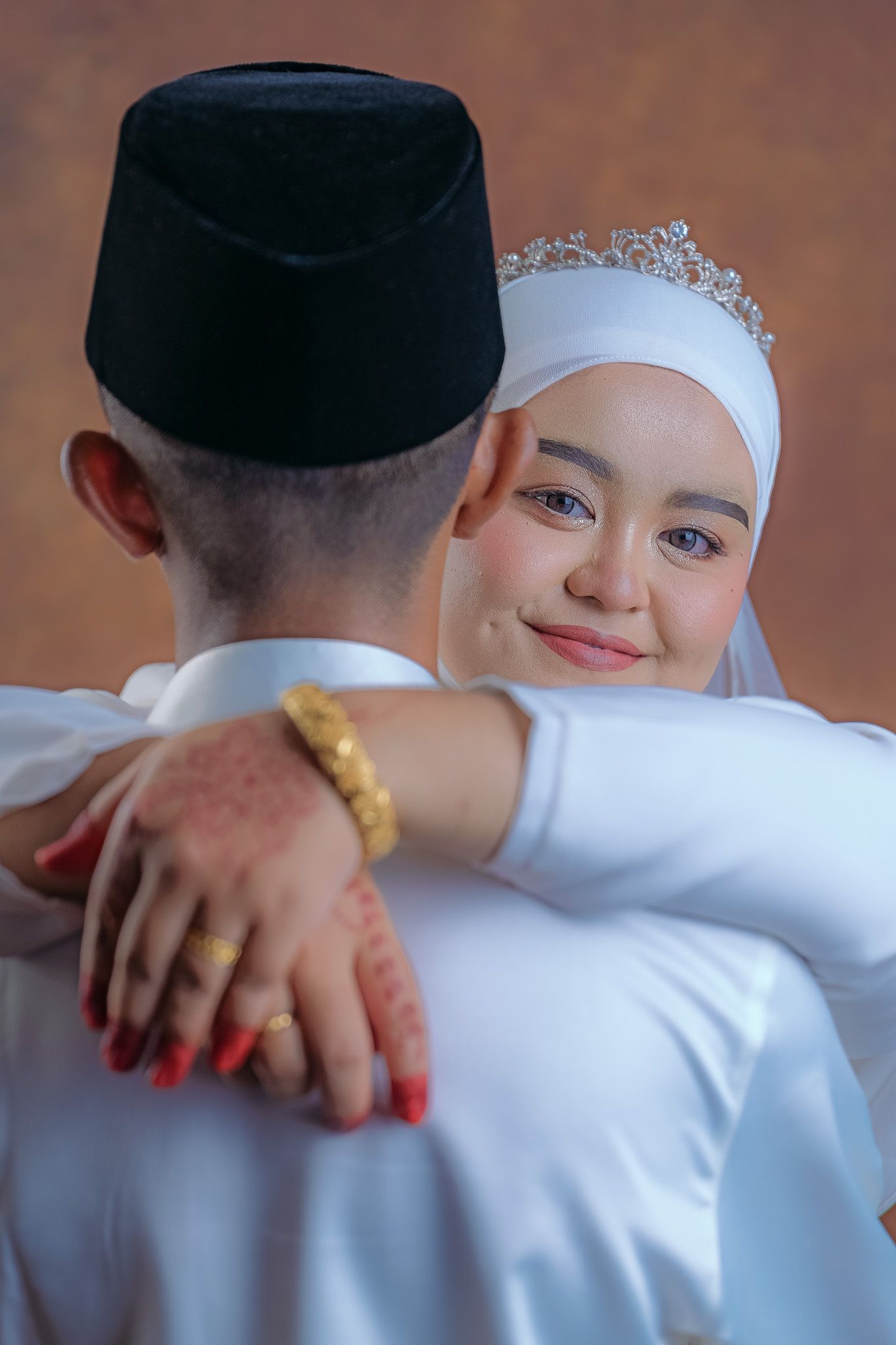 Close-up of newlyweds in traditional Malay wedding attire embracing during photo session.
